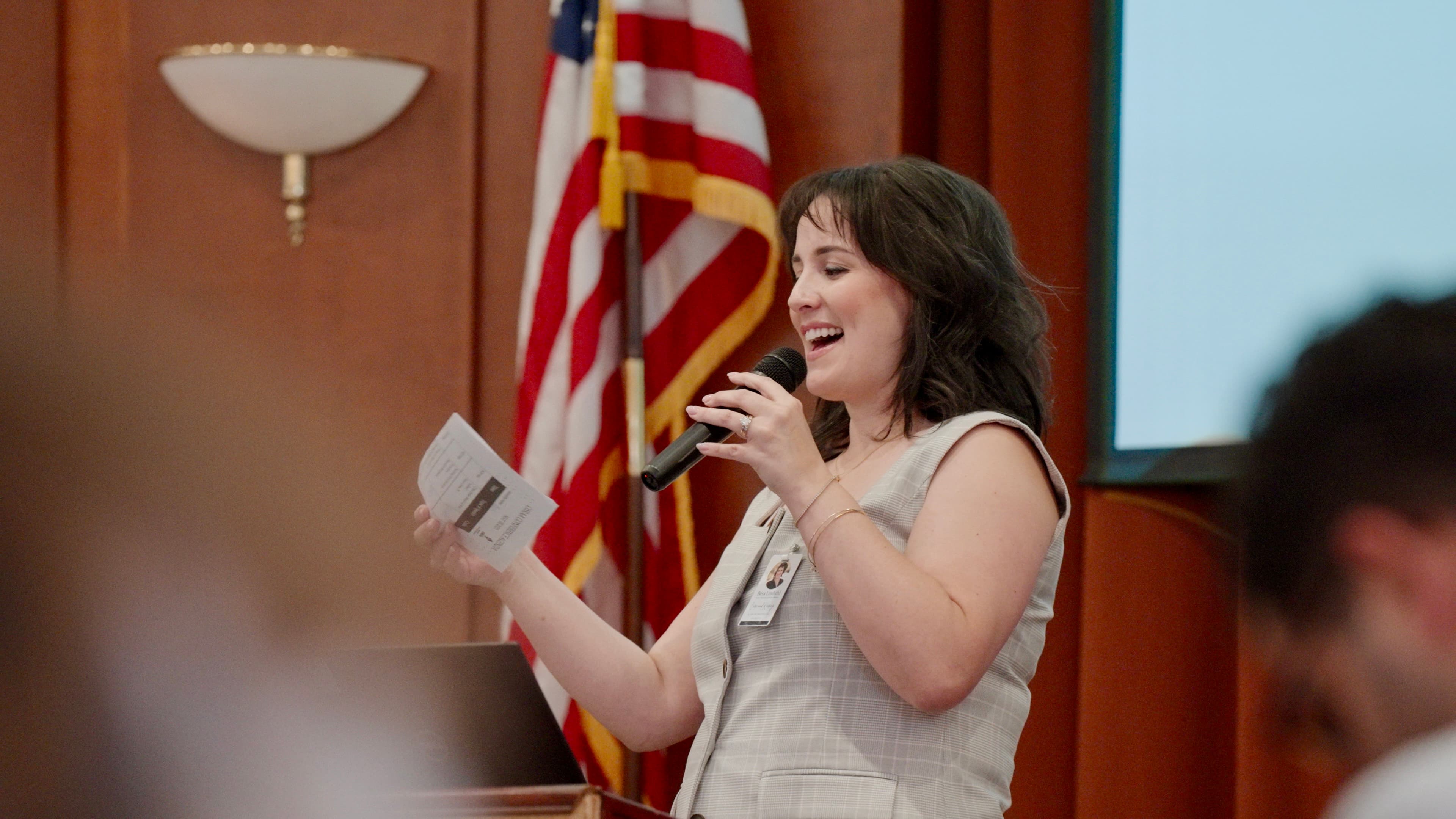 Conference emcee speaking into microphone with American flag in background